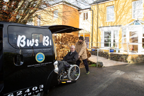 A man in a wheelchair being helped onto a bus funded by Brechfa Forest West Wind Farm